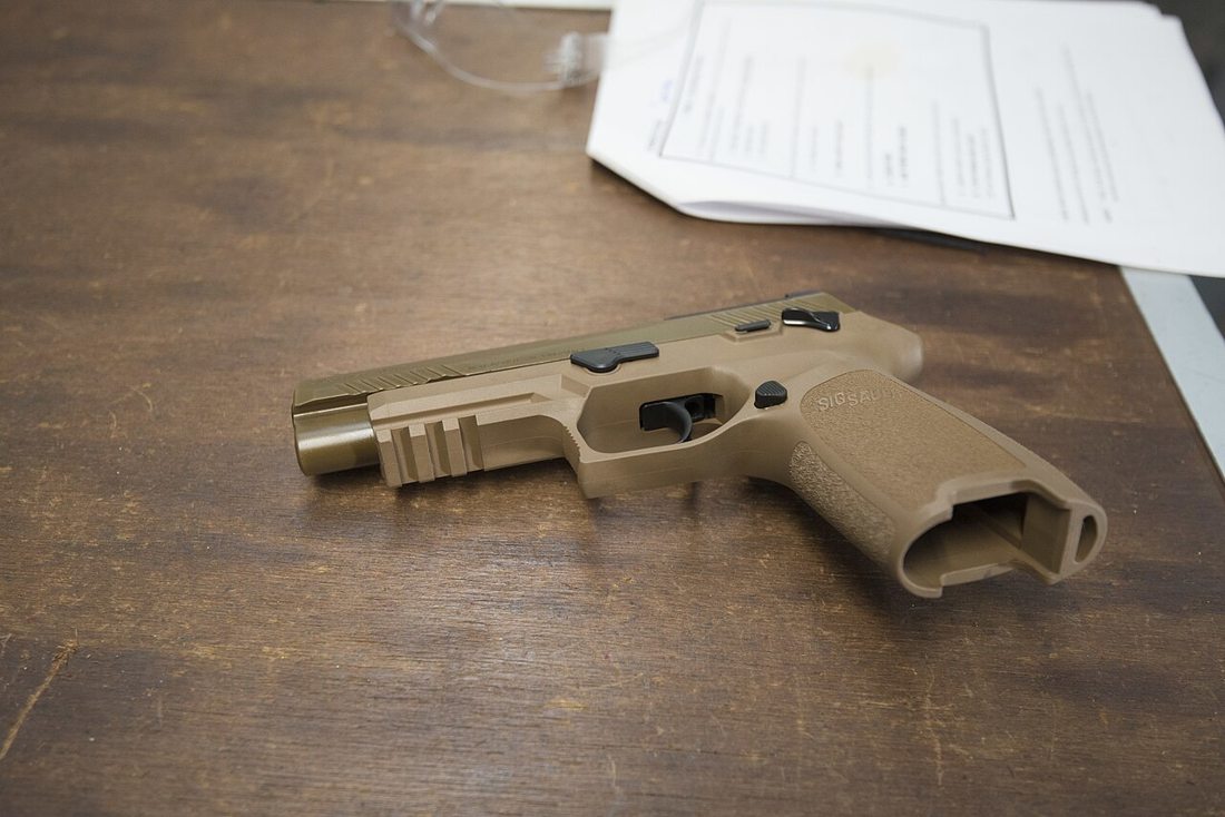 Pistola militar M17 apoyada sobre una mesa de madera durante una exhibición
